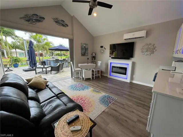 Living room featuring dark wood-type flooring, high vaulted ceiling, an AC wall unit, and ceiling fan