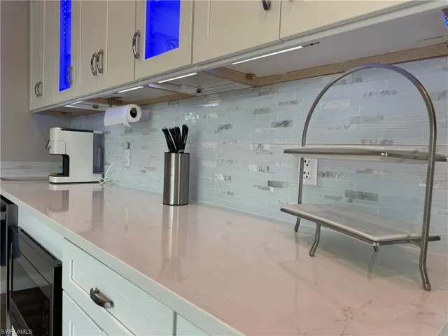Kitchen with light stone countertops, backsplash, stainless steel microwave, and white cabinets