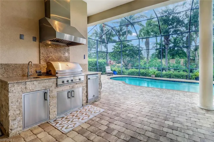 View of swimming pool featuring area for grilling, sink, a grill, a patio area, and glass enclosure