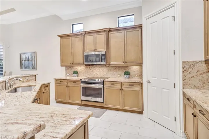 Kitchen with stainless steel appliances, sink, decorative backsplash, light tile patterned flooring, and ornamental molding