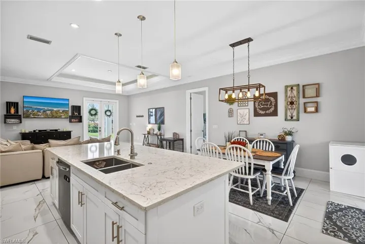 Kitchen featuring white cabinetry, light stone counters, open floor plan, ornamental molding, and a center island with sink
