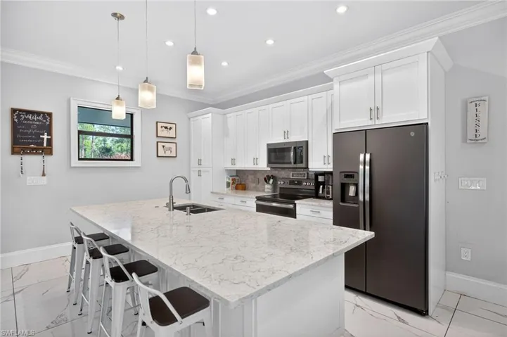 Kitchen with stainless steel appliances, white cabinets, a breakfast bar, light stone counters, and an island with sink