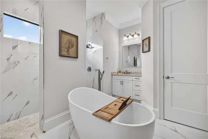 Bathroom featuring crown molding, vanity, a marble finish shower, and a freestanding tub