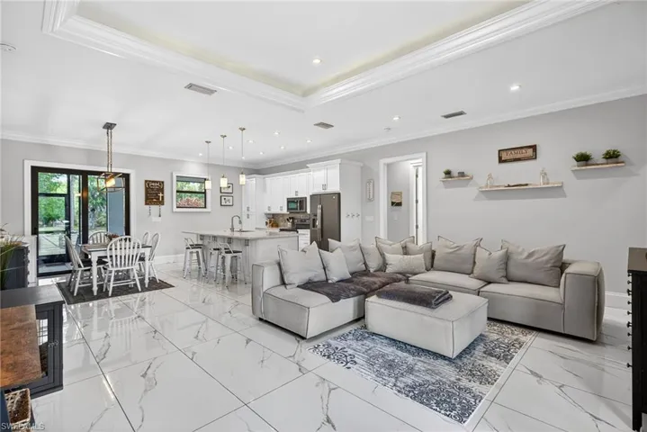 Living room with ornamental molding, recessed lighting, a tray ceiling, and light marble finish floors