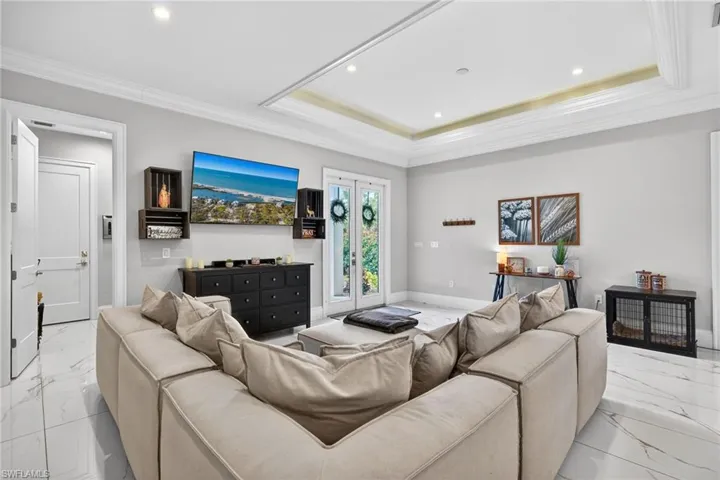 Living room featuring light marble finish flooring, crown molding, recessed lighting, and a raised ceiling