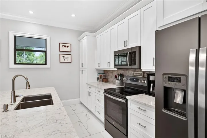 Kitchen with stainless steel appliances, light stone counters, crown molding, white cabinets, and light marble finish floors