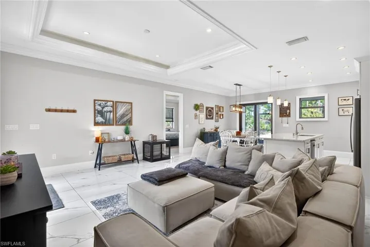 Living area with ornamental molding, light marble finish floors, and suspended lighting
