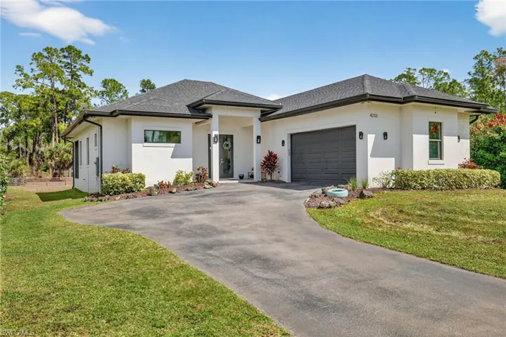 Prairie-style house with an attached garage, a front yard, driveway, stucco siding, and a shingled roof