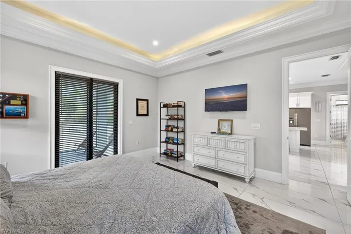Bedroom with ornamental molding, light marble finish flooring, stainless steel fridge, and a tray ceiling