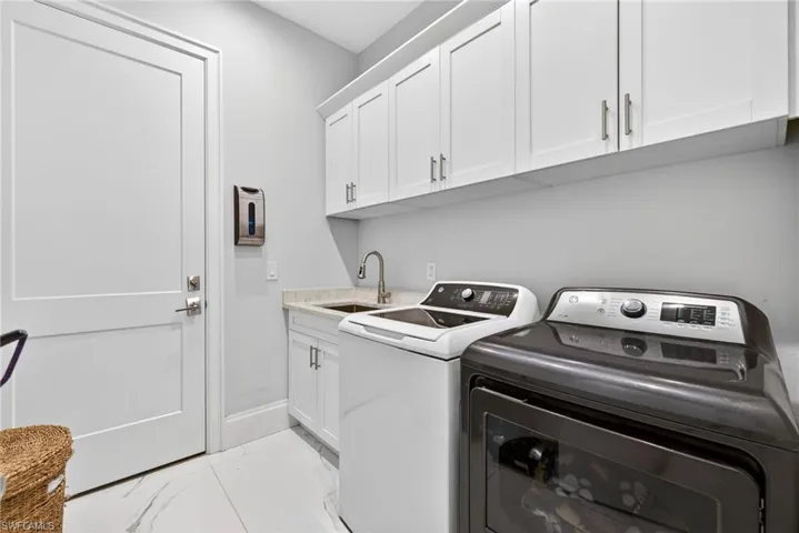 Laundry area with cabinet space, washing machine and clothes dryer, and light marble finish flooring
