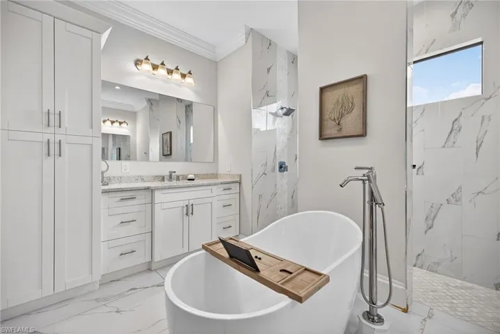 Full bath featuring ornamental molding, a marble finish shower, vanity, a freestanding tub, and light marble finish flooring