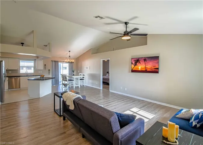 Living room with ceiling fan with notable chandelier, lofted ceiling, sink, and light wood-type flooring