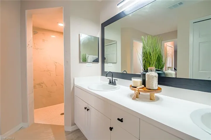 Bathroom featuring dual sinks, tiled shower, and large vanity