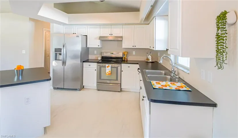 Kitchen with a tray ceiling, white cabinets, sink, light tile floors, and appliances with stainless steel finishes
