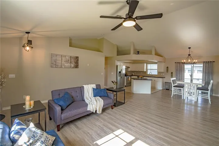 Living room featuring sink, ceiling fan with notable chandelier, light hardwood / wood-style flooring, and vaulted ceiling
