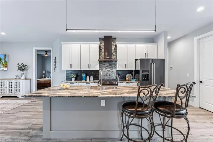 Kitchen featuring a breakfast bar area, wall chimney range hood, light stone countertops, an island with sink, and high quality fridge