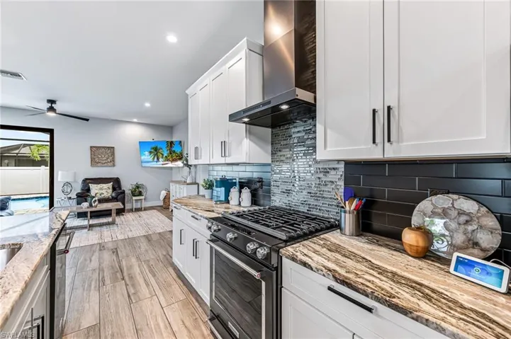 Kitchen with backsplash, black gas range, wall chimney exhaust hood, and light stone counters