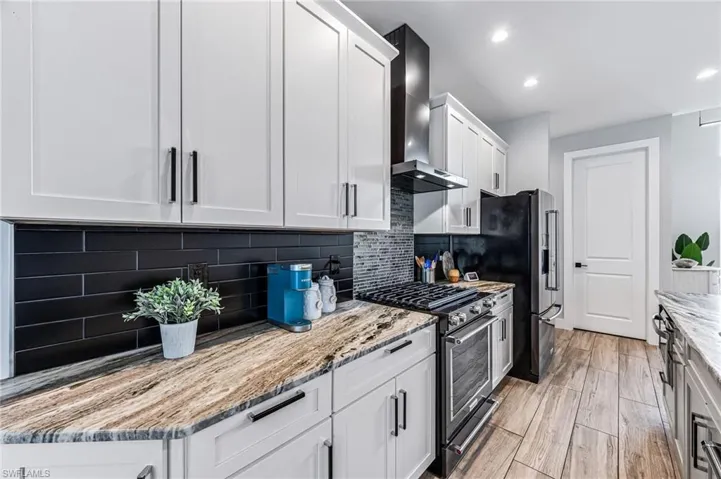 Kitchen featuring white cabinets, wall chimney exhaust hood, light stone countertops, high quality appliances, and backsplash
