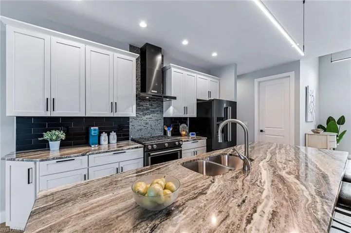 Kitchen with range with gas stovetop, wall chimney range hood, sink, backsplash, and white cabinetry