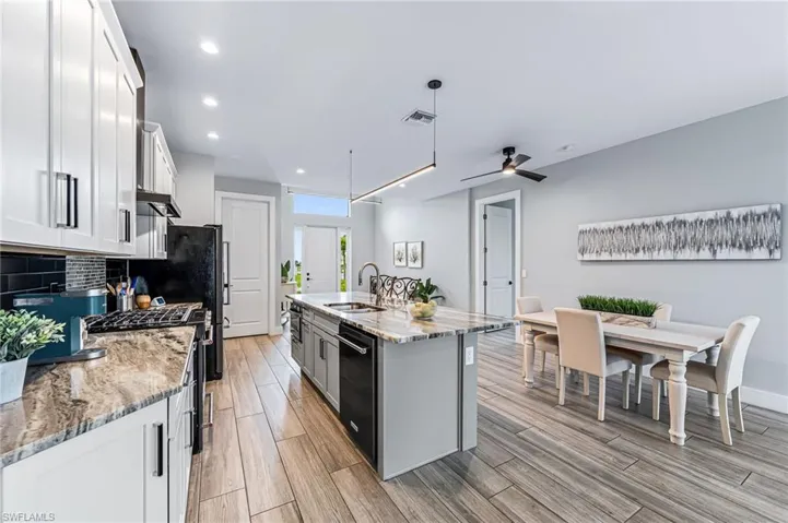 Kitchen with stainless steel stove, white cabinets, ceiling fan, an island with sink, and decorative backsplash