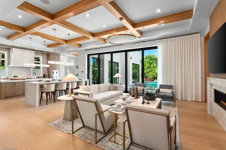 Living area featuring light wood-style flooring, a warm lit fireplace, beam ceiling, and coffered ceiling