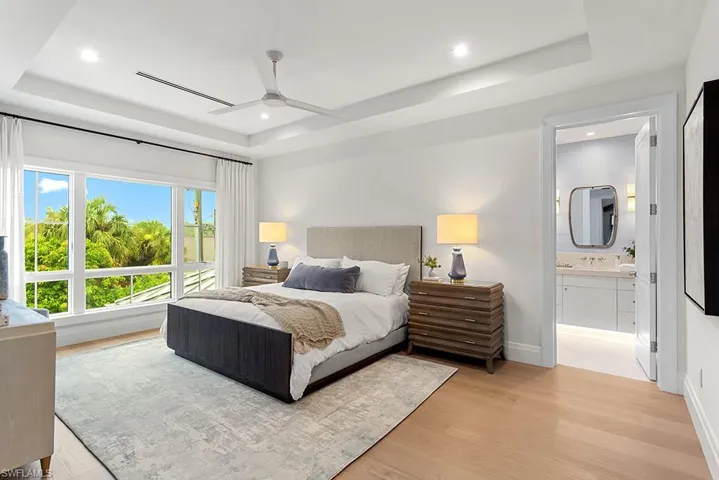 Bedroom featuring a raised ceiling, light wood finished floors, recessed lighting, ensuite bathroom, and ceiling fan