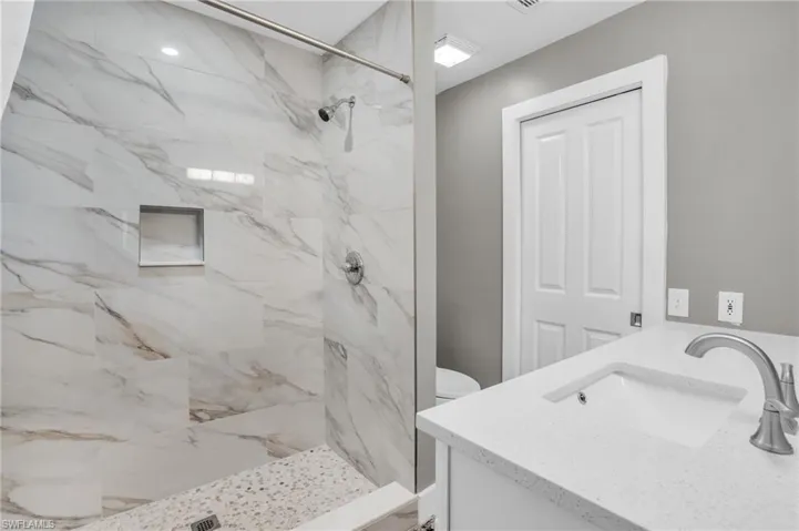 Bathroom featuring tiled shower, vanity, and toilet