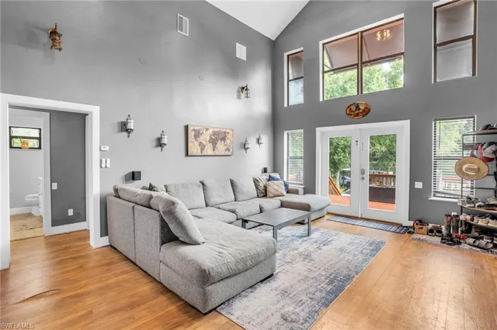 Living room with french doors, high vaulted ceiling, and light hardwood / wood-style flooring