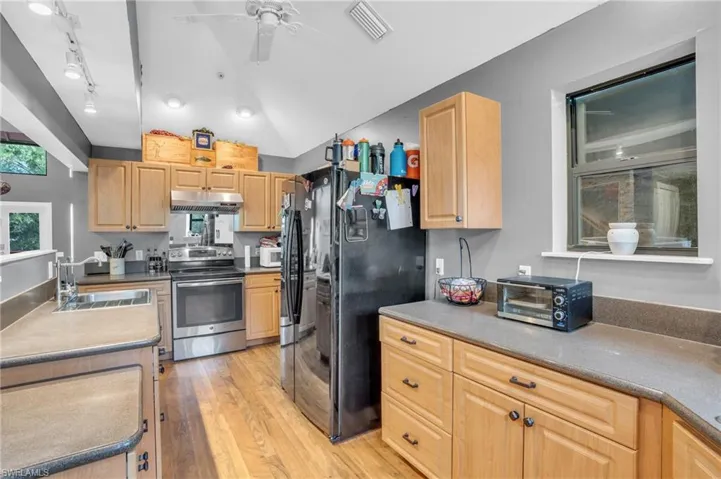 Kitchen with light wood-type flooring, stainless steel electric range oven, sink, ceiling fan, and black fridge