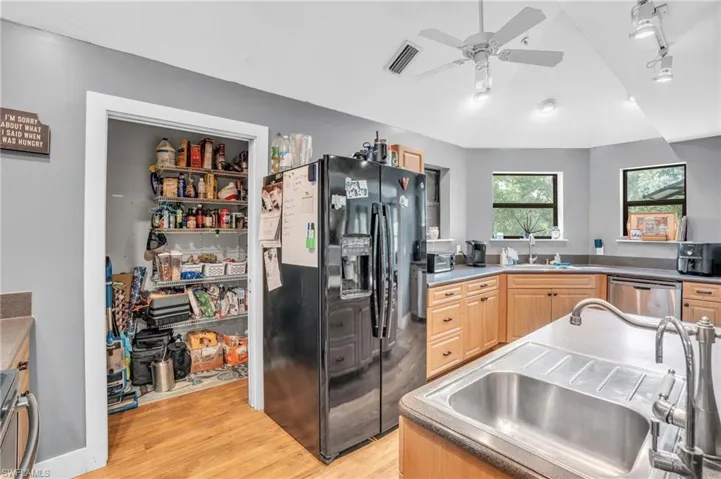 Kitchen with light wood-type flooring, dishwasher, ceiling fan, black refrigerator with ice dispenser, and light brown cabinets