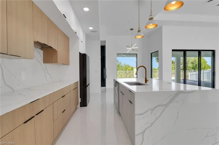 Kitchen with modern cabinets, light brown cabinetry, backsplash, freestanding refrigerator, and recessed lighting