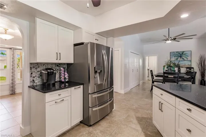 Kitchen with ceiling fan, tasteful backsplash, light tile flooring, stainless steel refrigerator with ice dispenser, and white cabinetry