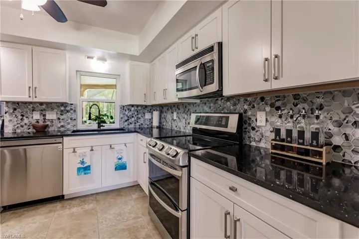 Kitchen featuring stainless steel appliances, sink, white cabinetry, and ceiling fan