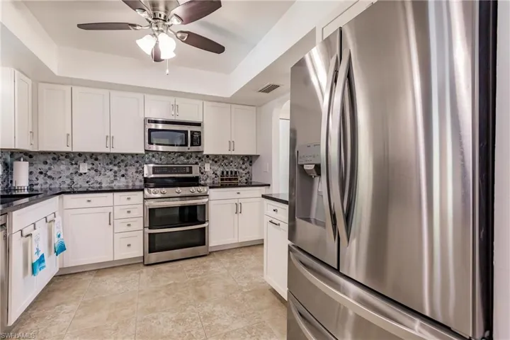 Kitchen featuring appliances with stainless steel finishes, white cabinets, backsplash, ceiling fan, and a raised ceiling