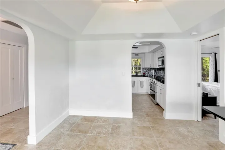 Kitchen featuring stainless steel appliances, backsplash, a tray ceiling, white cabinets, and light tile floors