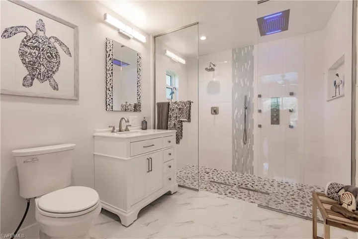 Bathroom with tile flooring, tiled shower, toilet, and vanity