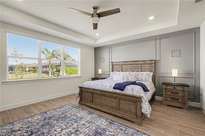 Bedroom with wood finish floors, ceiling fan, recessed lighting, a tray ceiling, and a decorative wall