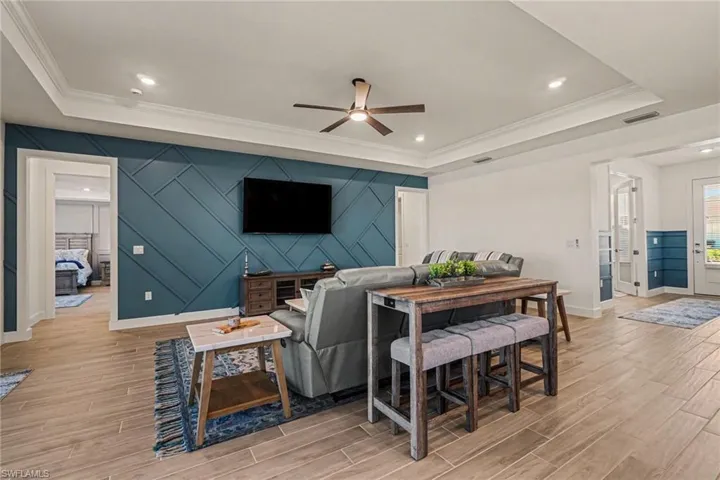 Living room featuring an accent wall, wood finish floors, ceiling fan, crown molding, and a decorative wall