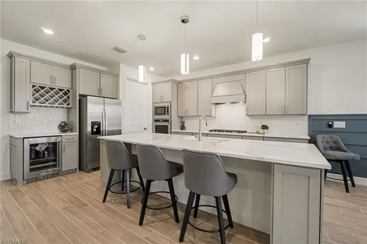 Kitchen with gray cabinets, stainless steel appliances, wood tiled floors, and pendant lighting