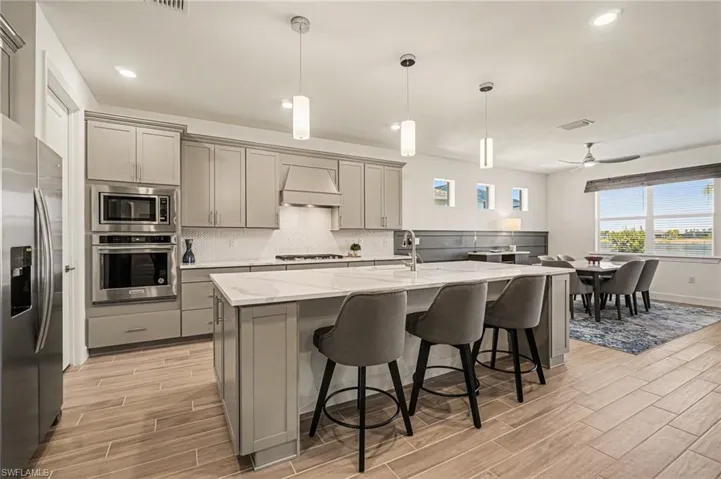 Kitchen with gray cabinetry, stainless steel appliances, wood tiled floors, and decorative light fixtures