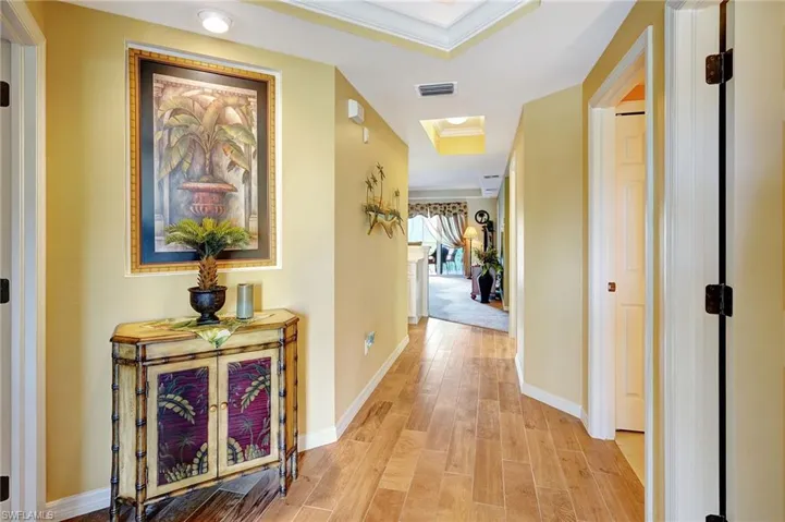 Hall featuring visible vents, baseboards, ornamental molding, light wood-type flooring, and a raised ceiling