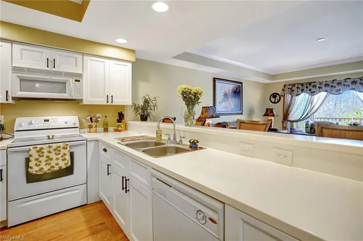 Kitchen featuring white appliances, white cabinets, light countertops, light wood-type flooring, and a sink