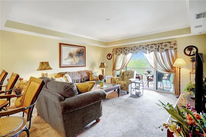 Carpeted living room featuring ornamental molding, a tray ceiling, and visible vents