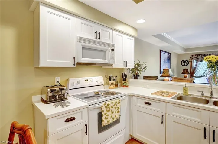 Kitchen with light countertops, white appliances, a sink, and white cabinetry
