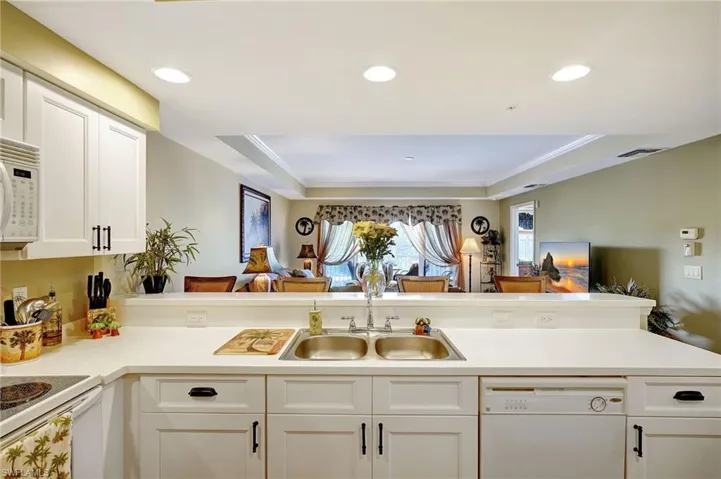 Kitchen with white appliances, a sink, white cabinets, open floor plan, and light countertops