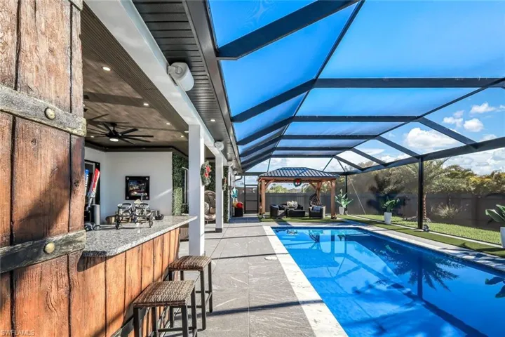 View of swimming pool with glass enclosure, a patio, a fenced in pool, ceiling fan, and outdoor dry bar
