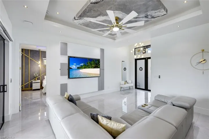 Living area with baseboards, recessed lighting, ceiling fan with notable chandelier, marble finish floor, and a raised ceiling