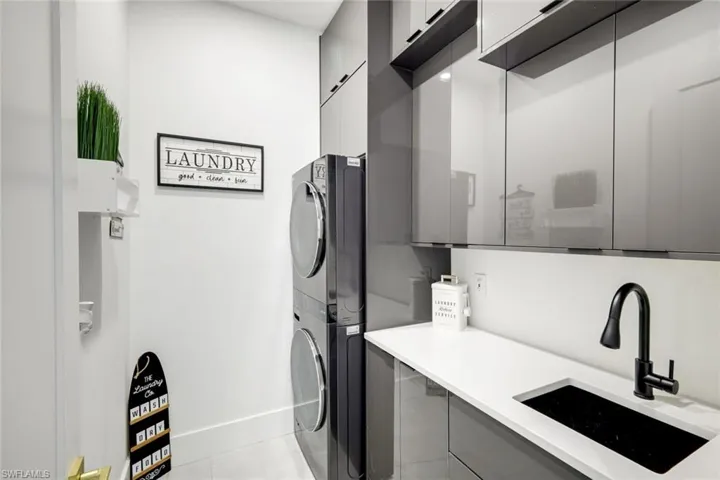 Laundry area featuring cabinet space, stacked washing maching and dryer, baseboards, and a sink