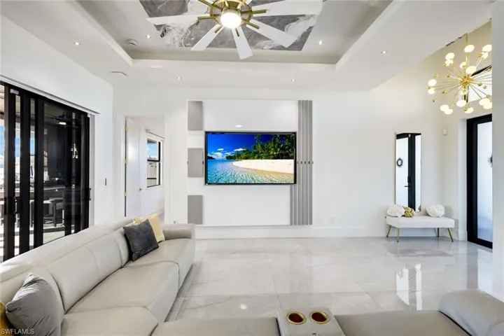 Living room featuring baseboards, recessed lighting, a raised ceiling, ceiling fan with notable chandelier, and marble finish floor