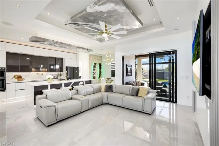 Living room with a raised ceiling, visible vents, marble finish floor, and ceiling fan